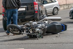 Broken motorcycle closeup beside a car during a road accident.